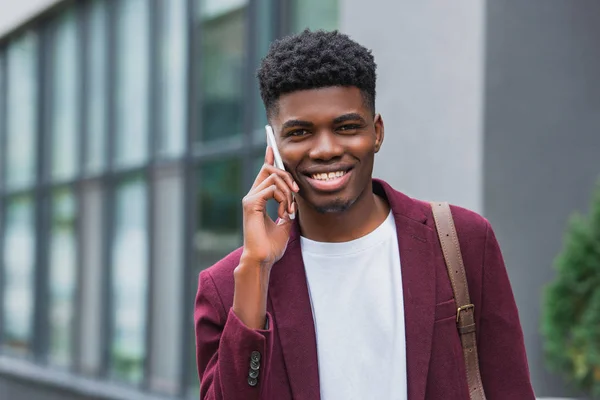 Close-up shot of smiling young man talking by phone on street and looking at camera — Stock Photo