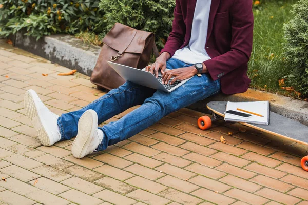 Cropped shot of freelancer using laptop while sitting on curb on street — Stock Photo