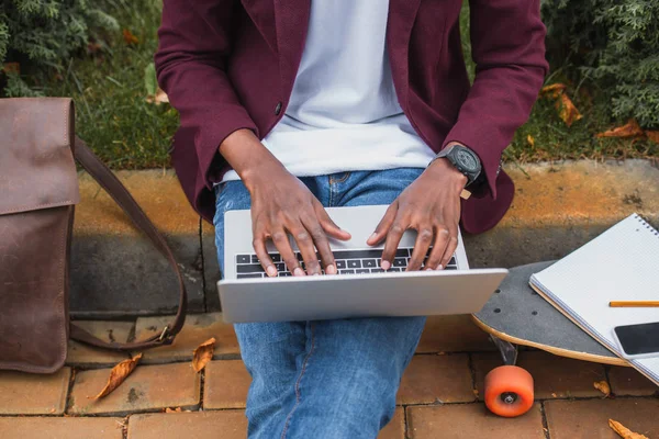 Tiro recortado de jovem freelancer usando laptop enquanto sentado no passeio na rua — Fotografia de Stock