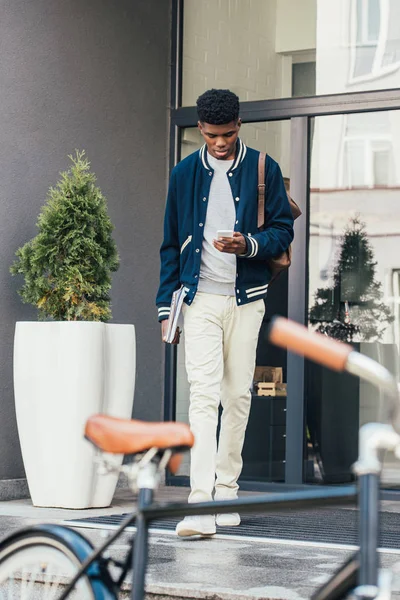 African american freelancer with documents using smartphone and going to bicycle — Stock Photo