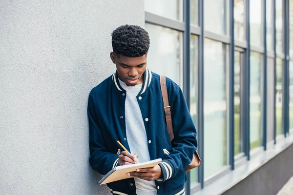 Jovem estudante afro-americano concentrado escrevendo em livro didático — Fotografia de Stock