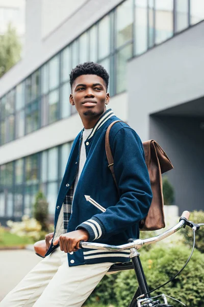 Heureux homme afro-américain élégant avec sac à dos en cuir appuyé sur le vélo — Photo de stock