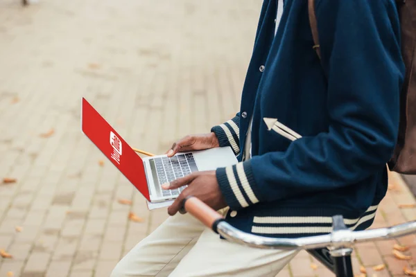 Cropped view of african american man laptop with youtube website while leaning on bike — Stock Photo