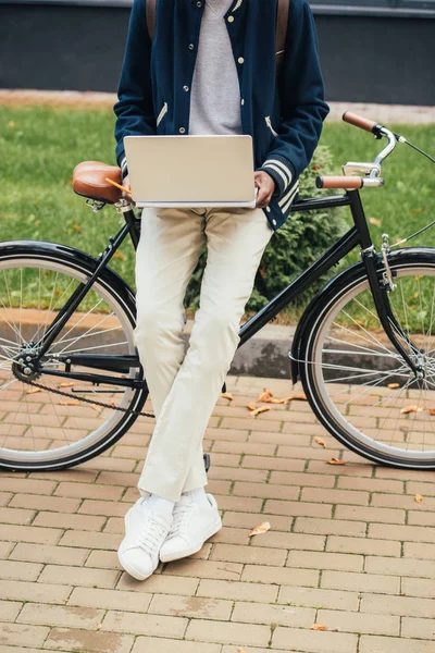 Vista recortada del freelancer afroamericano que trabaja con computadora portátil mientras se apoya en la bicicleta - foto de stock