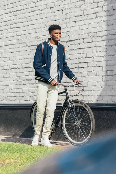 Hombre afroamericano de pie con bicicleta cerca de la pared de ladrillo blanco - foto de stock