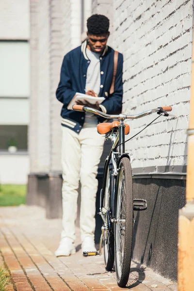 Messa a fuoco selettiva dei documenti di scrittura freelance afro-americani e in piedi in bicicletta sulla strada — Foto stock