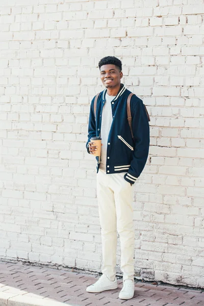 Stylish african american man holding coffee to go near white brick wall — Stock Photo