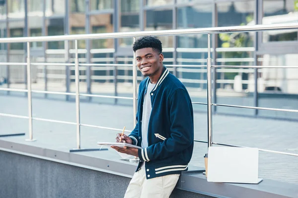 Freelancer afro-americano sorridente trabalhando com documentos na cidade com laptop — Stock Photo