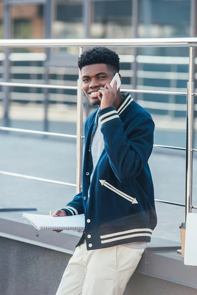 Freelancer afro-americano sorridente com documentos falando em smartphone na cidade — Fotografia de Stock