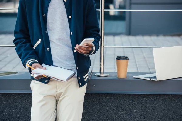 Vista cortada de freelancer com documentos, smartphone, laptop e café para ir na cidade — Fotografia de Stock