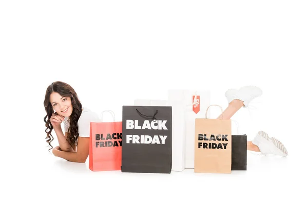 Schönes lächelndes Mädchen, das an Einkaufstaschen mit schwarzen Freitagssymbolen liegt, isoliert auf weißem Grund — Stockfoto