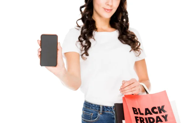 Vue recadrée de fille montrant smartphone avec écran vide et tenant des sacs à provisions avec panneau noir vendredi isolé sur blanc — Photo de stock