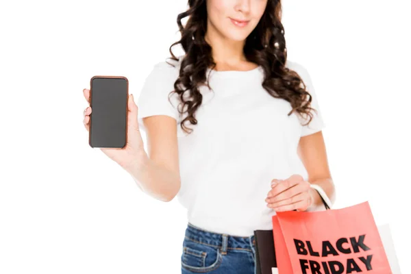 Cropped view of girl showing smartphone with blank screen and holding shopping bags with black friday sign isolated on white — Stock Photo