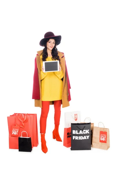 Belo shopaholic apresentando tablet com tela em branco perto de sacos de compras com sinais de sexta-feira preto isolado no branco — Fotografia de Stock