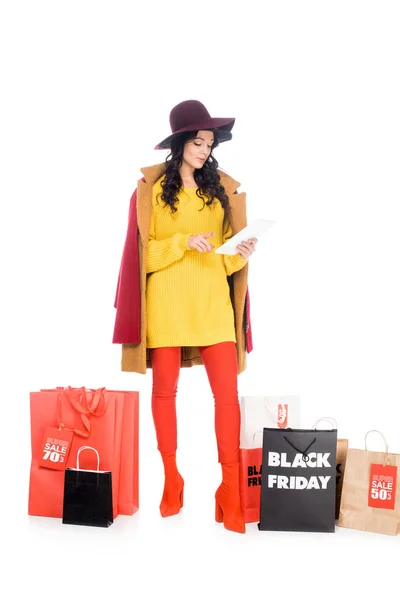 Shopaholic atraente usando tablet digital perto de sacos de compras com sinais de sexta-feira preto isolado em branco — Fotografia de Stock