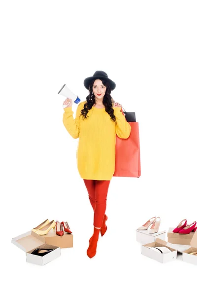 Beautiful shopaholic holding megaphone and shopping bags isolated on white with footwear — Stock Photo