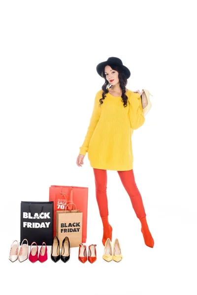 Стильна жінка стоїть поруч з сумками з чорною п'ятницею та організовує жіноче взуття ізольовано на білому — стокове фото