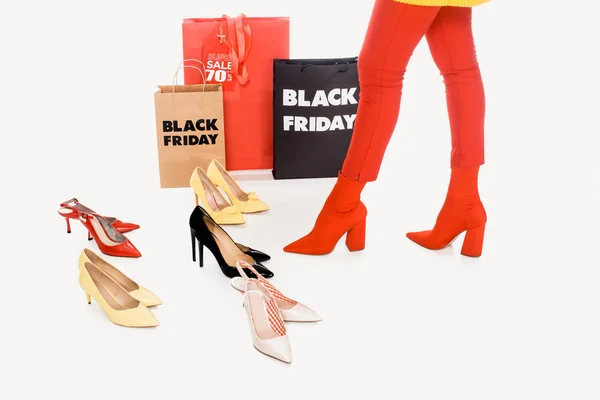 Partial view of woman, shopping bags with black friday inscription and stylish female footwear isolated on white — Stock Photo