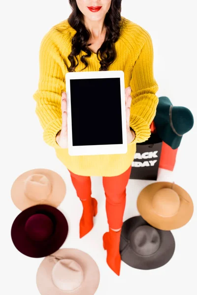 Mulher elegante mostrando tablet com tela em branco nas mãos, chapéus e sacos de compras em torno isolado no branco — Fotografia de Stock
