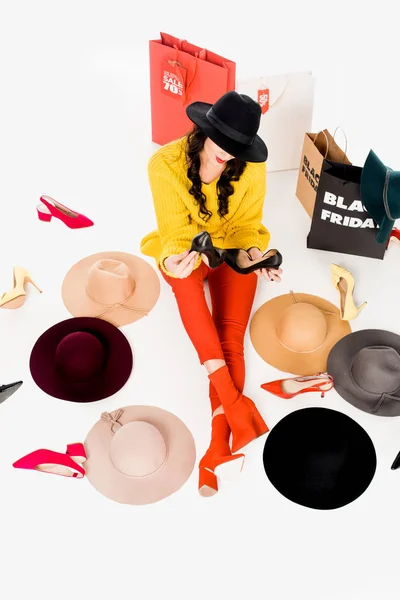 Hochwinkelaufnahme einer Frau, die mit Schuhen, Hüten und Einkaufstaschen mit schwarzer Freitag-Schrift auf dem Boden sitzt, vereinzelt auf weißem Grund — Stockfoto