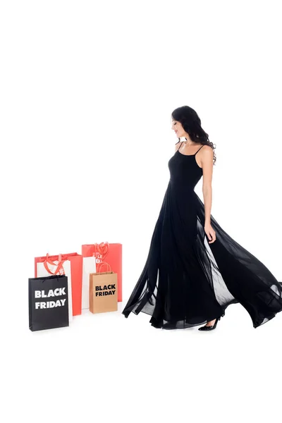 Hermosa mujer en vestido negro mirando las bolsas de compras con letras de viernes negro aislado en blanco - foto de stock