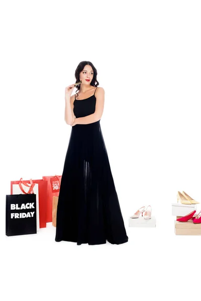 Young woman holding credit card with shopping bags and female shoes behind isolated on white, black friday sale concept — Stock Photo