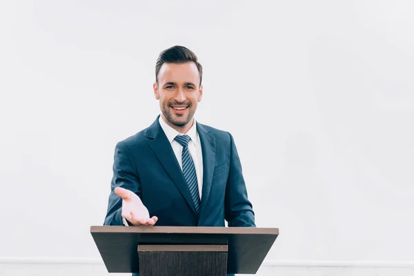 Conférencier souriant debout et gestuelle au podium tribune pendant le séminaire dans la salle de conférence — Photo de stock