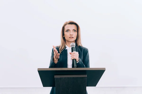 Schöner Redner gestikuliert und spricht ins Mikrofon auf der Podiumstribüne während des Seminars im Konferenzsaal — Stockfoto