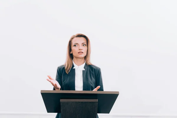 Attractive speaker gesturing and talking at podium tribune during seminar in conference hall — Stock Photo