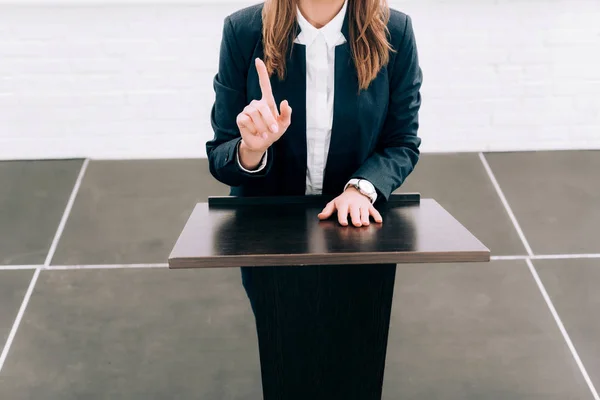 Imagem cortada de palestrante mostrando um dedo para cima no tribuno pódio durante o seminário na sala de conferências — Fotografia de Stock