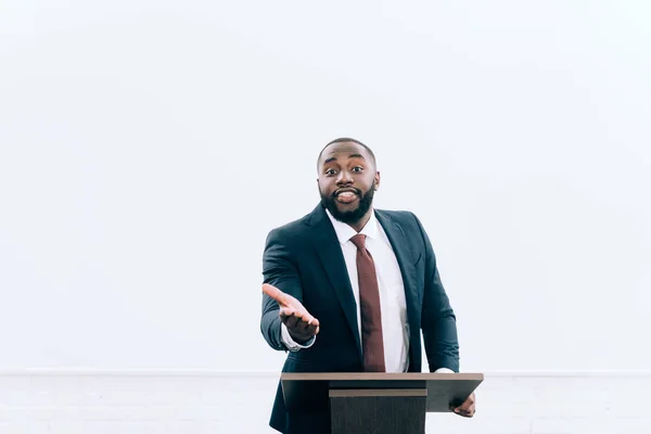 Beau conférencier afro-américain debout sur le podium tribune et gestuelle pendant le séminaire dans la salle de conférence — Photo de stock