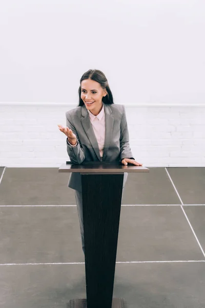 Vue en grand angle d'un beau conférencier souriant faisant un geste au podium tribune lors d'un séminaire dans une salle de conférence — Photo de stock