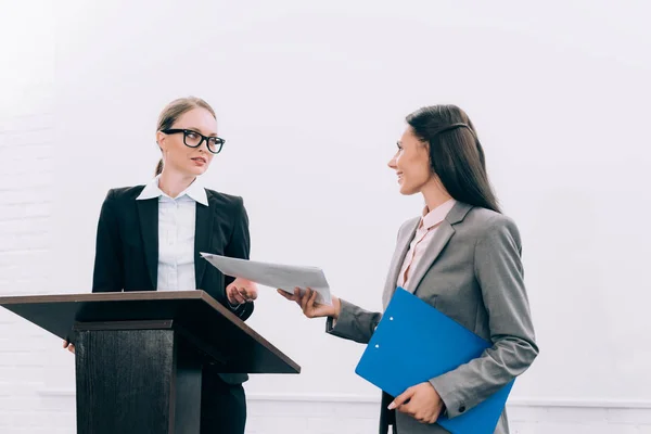 Belle assistante donnant des documents à un conférencier attrayant pendant le séminaire en salle de conférence — Photo de stock