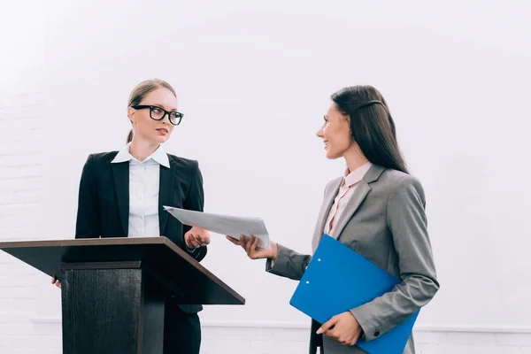 Schöner Assistent, der attraktiven Rednerin während des Seminars im Konferenzsaal Dokumente überreicht — Stockfoto