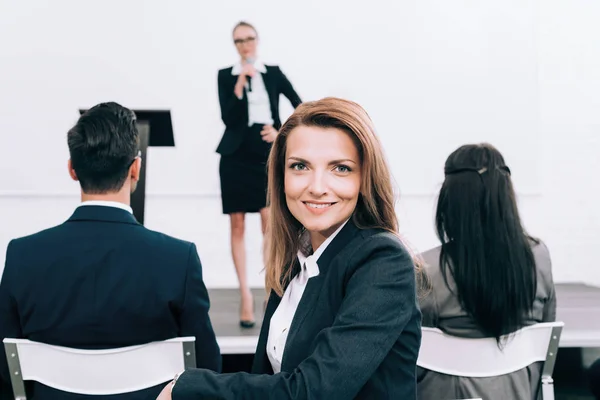 Lächelnde Geschäftsfrau blickt während eines Seminars im Konferenzsaal in die Kamera — Stockfoto