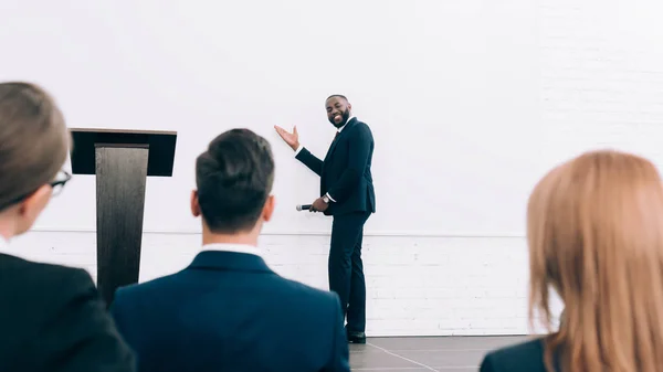 Sorrindo bonito orador afro-americano falando durante o seminário na sala de conferências e apontando na tela — Fotografia de Stock