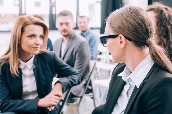 Selective focus of attractive businesswomen sitting on chairs and talking in conference hall — Stock Photo