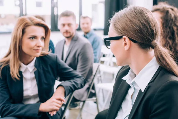 L'accent sélectif des femmes d'affaires attrayantes assises sur des chaises et parlant dans la salle de conférence — Photo de stock