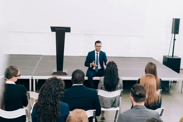 High angle view speaker sitting on stage during seminar in conference hall and talking to multicultural audience — Stock Photo