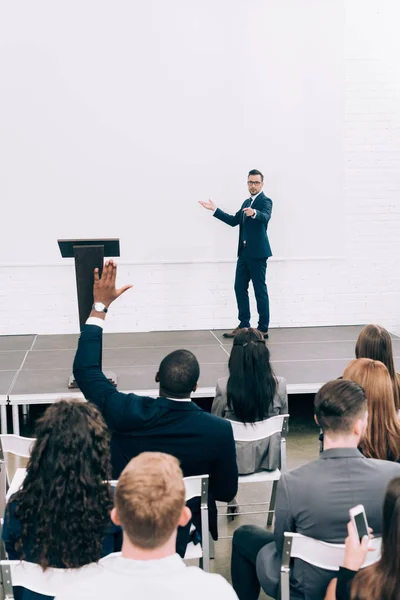 Participante afroamericano levantando la mano, conferenciante hablando con el público durante la presentación en la sala de conferencias - foto de stock