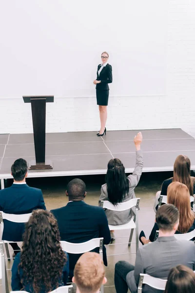 Vue en grand angle du conférencier regardant le public multiethnique pendant le séminaire dans la salle de conférence, participant levant la main — Photo de stock