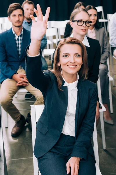 Sorridente empresária com mão para cima quer fazer pergunta durante seminário de negócios na sala de conferências — Fotografia de Stock