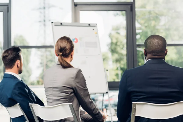 Vue arrière des gens d'affaires multiculturels assis dans la salle de conférence avec tableau blanc — Photo de stock