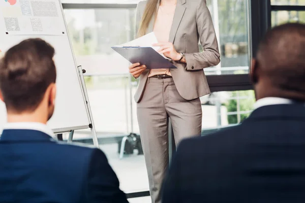 Partial view of female educator with notepad and multiracial business colleagues on seminar in conference hall — Stock Photo