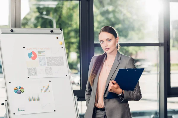 Female business speaker with notepad at white board during lecture in conference hall — Stock Photo