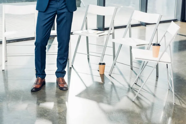 Vista parcial del hombre de negocios parado en sillas vacías en la sala de conferencias - foto de stock