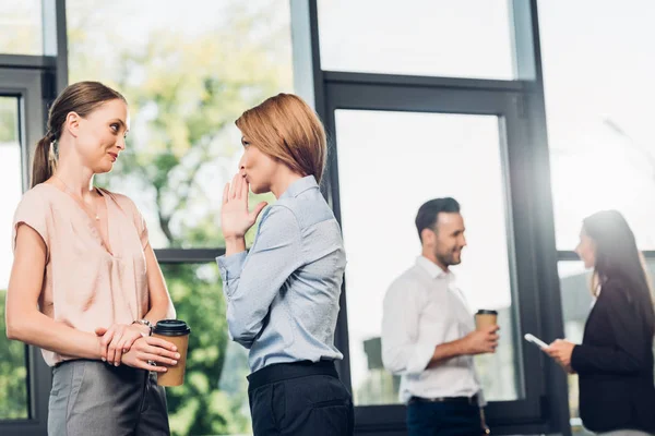 Бізнес-леді пліткує в той час як жінки мають розмову позаду в офісі — стокове фото