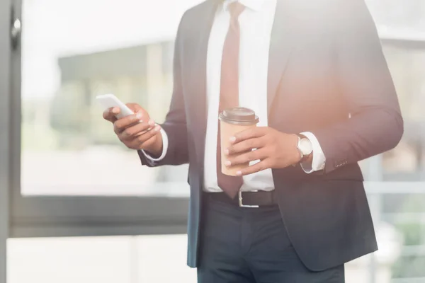 Partial view of african american businessman with coffee to go using smartphone in conference hall — Stock Photo