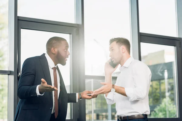 African american businessman looking at colleague talking on smartphone in conference hall — Stock Photo