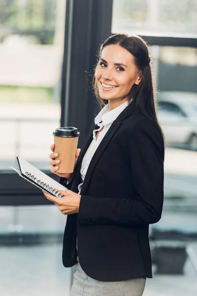 Vista lateral da jovem mulher de negócios sorridente com café para ir e notebook na sala de conferências — Fotografia de Stock